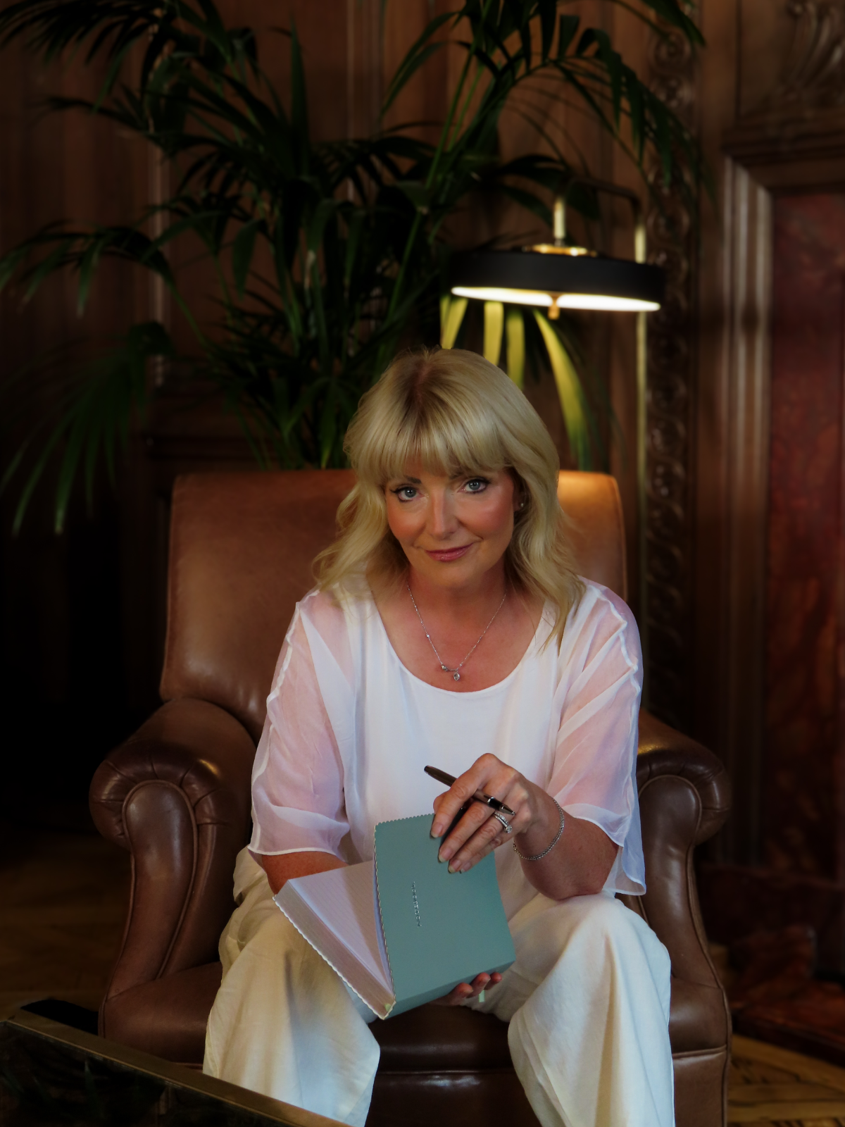 Dr Marie Meechan sitting on a leather bench in a cobalt blazer, smiling warmly, her research on infertility resting beside her.