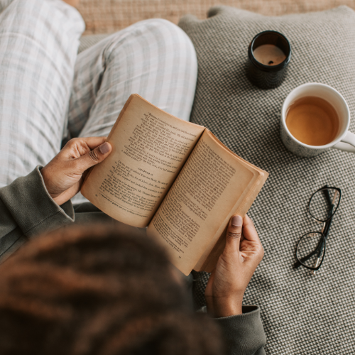 A practitioner reading quietly with a cup of tea, in soft natural light.