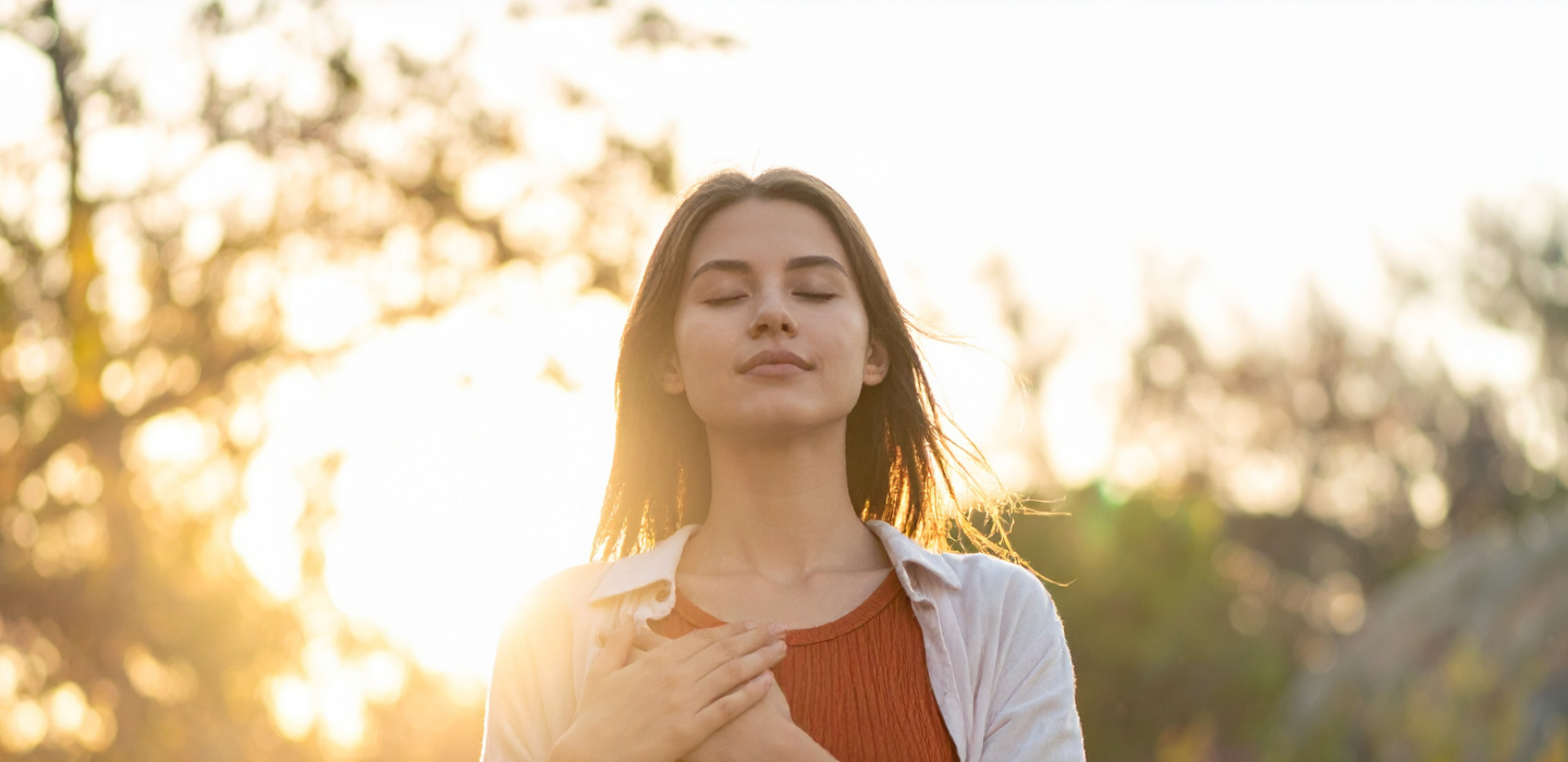 A person standing in golden light with hands resting over their heart.