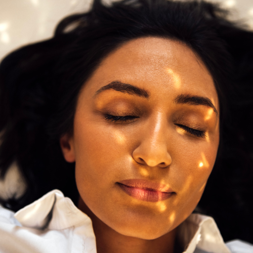 A person lying down with eyes closed, dappled golden light across their face.
